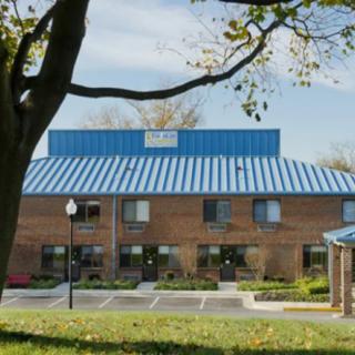 A brick building with a blue roof, surrounded by trees and a parking lot.