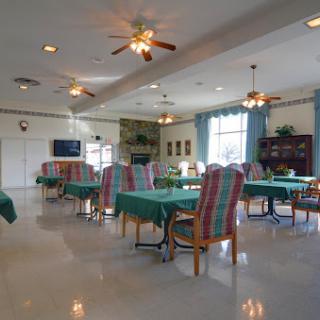 A spacious and brightly lit dining area designed for community gatherings, featuring tables covered with green cloth and comfortable seating.