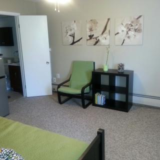 A tidy bedroom featuring a green chair, a black shelf with decor items, and floral artwork on the wall.