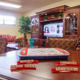 A cozy indoor setting featuring a Scrabble board on a table, with comfortable seating and a TV in the background.