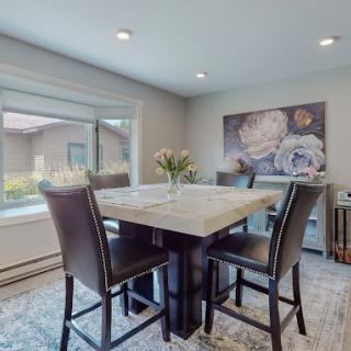 A modern dining room featuring a high table surrounded by chairs, adorned with a vase of flowers and complemented by wall artwork.