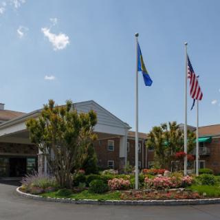 A welcoming hotel entrance surrounded by vibrant landscaping and flags.
