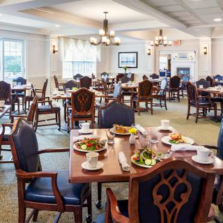 An elegant dining room setting with multiple tables prepared for guests, featuring neatly arranged chairs and plates of food.