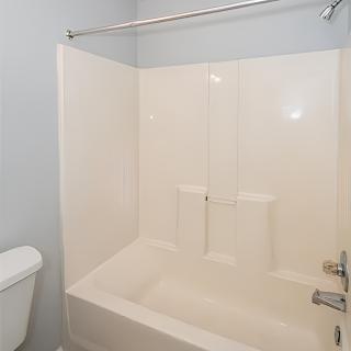 A clean and simple bathroom featuring a white bathtub with an integrated shower, alongside a toilet.