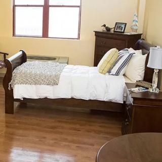 A cozy bedroom with a wooden bed frame and matching nightstand, featuring a comfortable bed with patterned pillows.