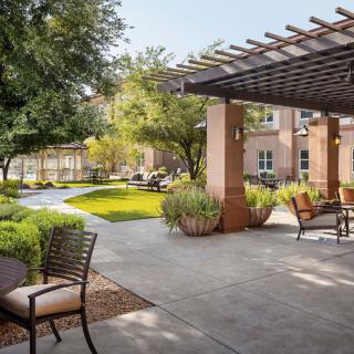 A serene garden with outdoor seating under a pergola, surrounded by lush greenery.