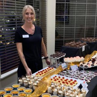 A person standing behind a table filled with various desserts and pastries at an event.