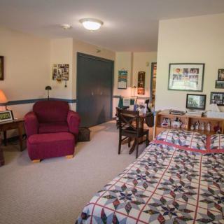 A cozy bedroom with a bed, desk, and chair, decorated with personal items and pictures.
