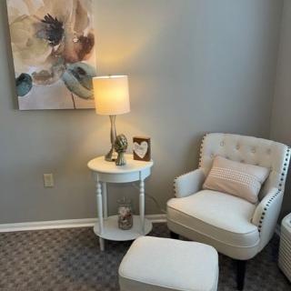 A cozy living room corner featuring a comfortable armchair, a side table with a lamp, and decorative artwork on the wall.
