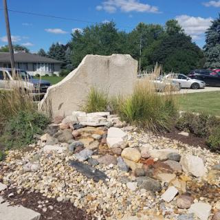 A peaceful garden landscape featuring a rock formation and various plants.