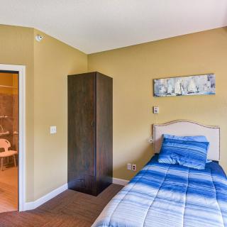 A simple bedroom featuring a single bed with blue bedding, a dark wardrobe, and minimalist decor.