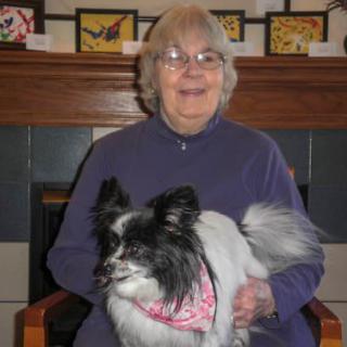 A woman smiling while holding a dog in front of a fireplace.