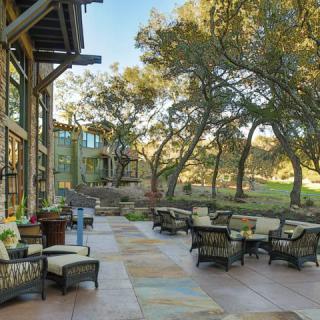 A spacious outdoor patio area surrounded by trees, featuring comfortable seating and a natural landscape.