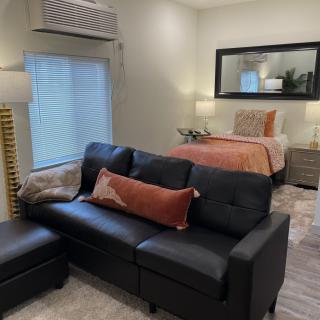 A modern studio apartment featuring a cozy living area with a black sofa and an adjacent bedroom space.