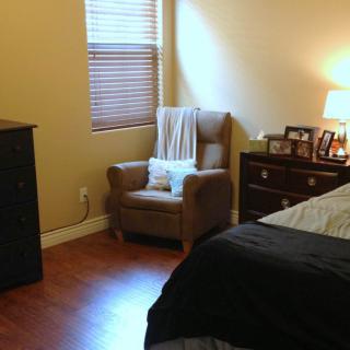 Cozy bedroom with a chair, dresser, and soft lighting.