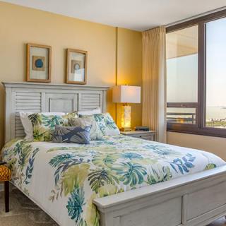 A cozy bedroom with floral bedding and large windows offering a view.