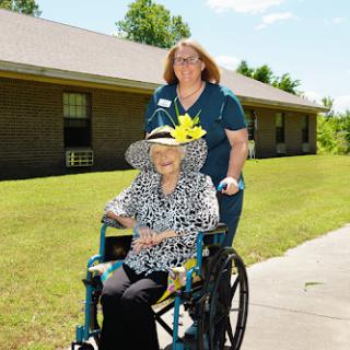 A caregiver assists an elderly woman in a wheelchair, enjoying a sunny day outdoors.