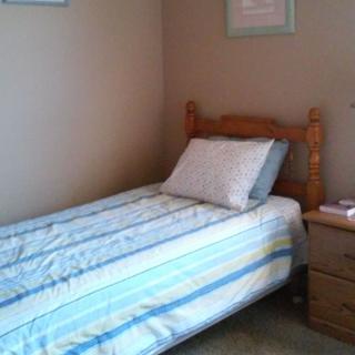 A small bedroom featuring a single bed with striped bedding and a wooden nightstand.