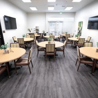 A spacious and modern dining room setup with circular tables and comfortable chairs, designed for gatherings and meetings.