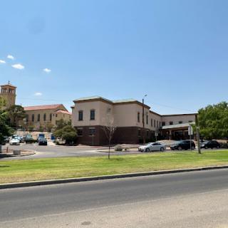 A view of a modern building with a parking lot under a clear blue sky.