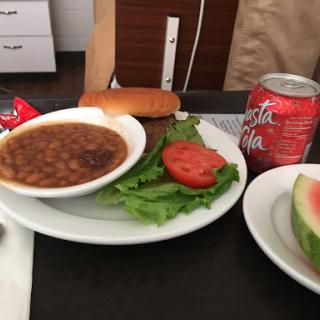 A simple meal featuring beans, salad with tomato, a soda, and watermelon on the side.