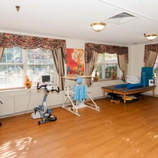 A rehabilitation room equipped with exercise machines and a wooden floor, designed for physical therapy.