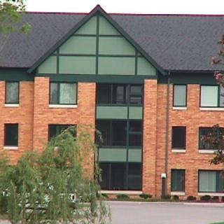 A modern brick building with large windows and green accents surrounded by trees.