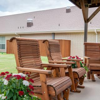 Wooden patio chairs under a shelter with flowers nearby.