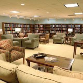 A cozy library reading area with bookshelves, armchairs, and sofas.