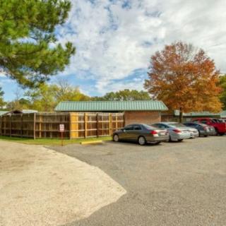 A small parking lot next to a building with several cars parked under a partly cloudy sky, surrounded by trees with autumn foliage.