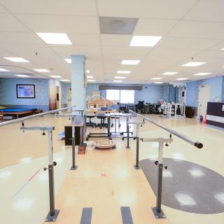 A spacious physical therapy room equipped with exercise equipment and parallel bars.