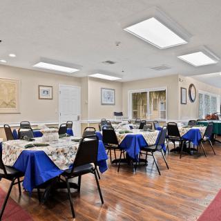 A spacious dining area with tables and chairs neatly arranged, featuring blue tablecloths on a hardwood floor.