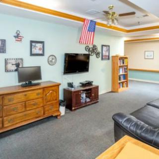 A cozy living room with a television, computer, wooden furniture, bookshelf, and decorative items including an American flag.