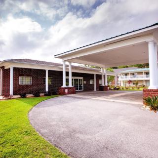 A well-maintained building entrance with white columns and a circular driveway under a partly cloudy sky.