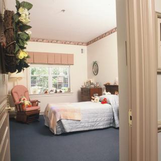 A cozy bedroom with a neatly made bed, armchair, and window offering natural light.