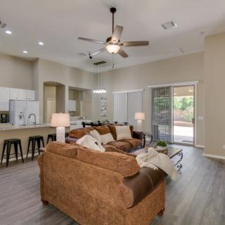 A spacious living room with an open floor plan, featuring a modern sofa, kitchen area with bar stools, and abundant natural light.