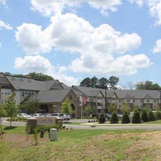 A scenic view of a building complex with trees, cars, and a cloudy sky.
