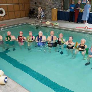 A group of seniors participating in a water aerobics class at an indoor swimming pool.