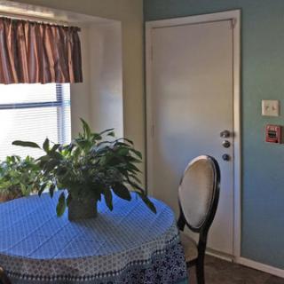 A cozy dining area featuring a round table with a blue tablecloth, a chair, and a potted plant, next to a door and window.