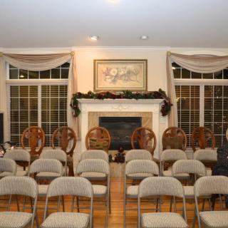 A living room set up with rows of chairs facing a decorated fireplace.