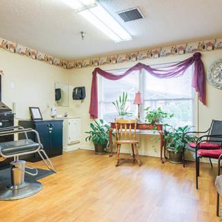A cozy salon with a waiting area and styling chair, featuring plants by the window.