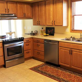 A cozy kitchen with wooden cabinets, stainless steel appliances, and a colorful rug.