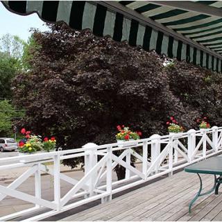 A scenic outdoor patio with a striped awning and white fence adorned with colorful flowers.
