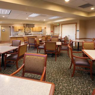 An empty dining room with neatly arranged tables and chairs, featuring warm lighting and a patterned carpet.