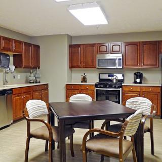 A modern kitchen with wooden cabinets, a central dining table, and stainless steel appliances.