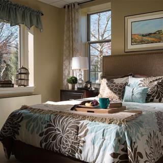 A cozy bedroom with elegant decor, featuring a neatly made bed, bedside lamp, and framed artwork above the headboard.