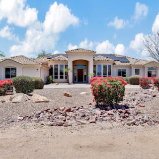 A beautiful residential home surrounded by well-maintained landscaping and a clear, sunny sky.