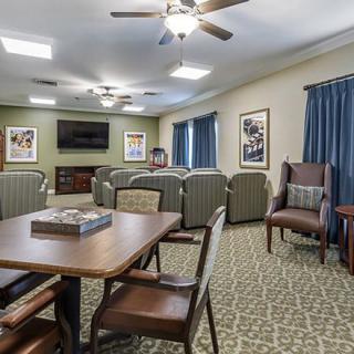 A cozy living room with comfortable seating, a television, tables, and chairs, decorated with artwork on the walls.