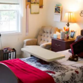 A cozy bedroom with a bed, side table, lamp, and an armchair by the window.