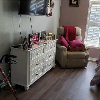 A cozy living room corner featuring a dresser with decorations, an armchair with red pillows, and a TV mounted on the wall.